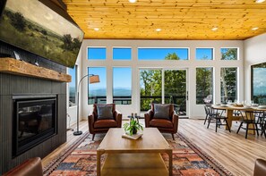 A modern living room with a fireplace, leather chairs, a coffee table, and large windows offering a view of the outdoors. - Dog|EV|Hot Tub|Pool Table|BBQ|Gas Fire|King Bed (Sevierville)