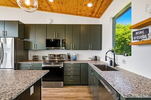 A modern kitchen with dark cabinets, stainless steel appliances, granite countertops, and a window with a view of greenery. - Dog|EV|Hot Tub|Pool Table|BBQ|Gas Fire|King Bed (Sevierville)