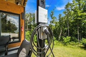 An electric vehicle charging station with a sign, a fire extinguisher, and a view of a forested area. - Dog|EV|Hot Tub|Pool Table|BBQ|Gas Fire|King Bed (Sevierville)