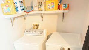 A laundry area with a washing machine and dryer, a shelf with detergent bottles, and a vent above the machines. - Windsor Retreat Private Basement Suite (Denver)