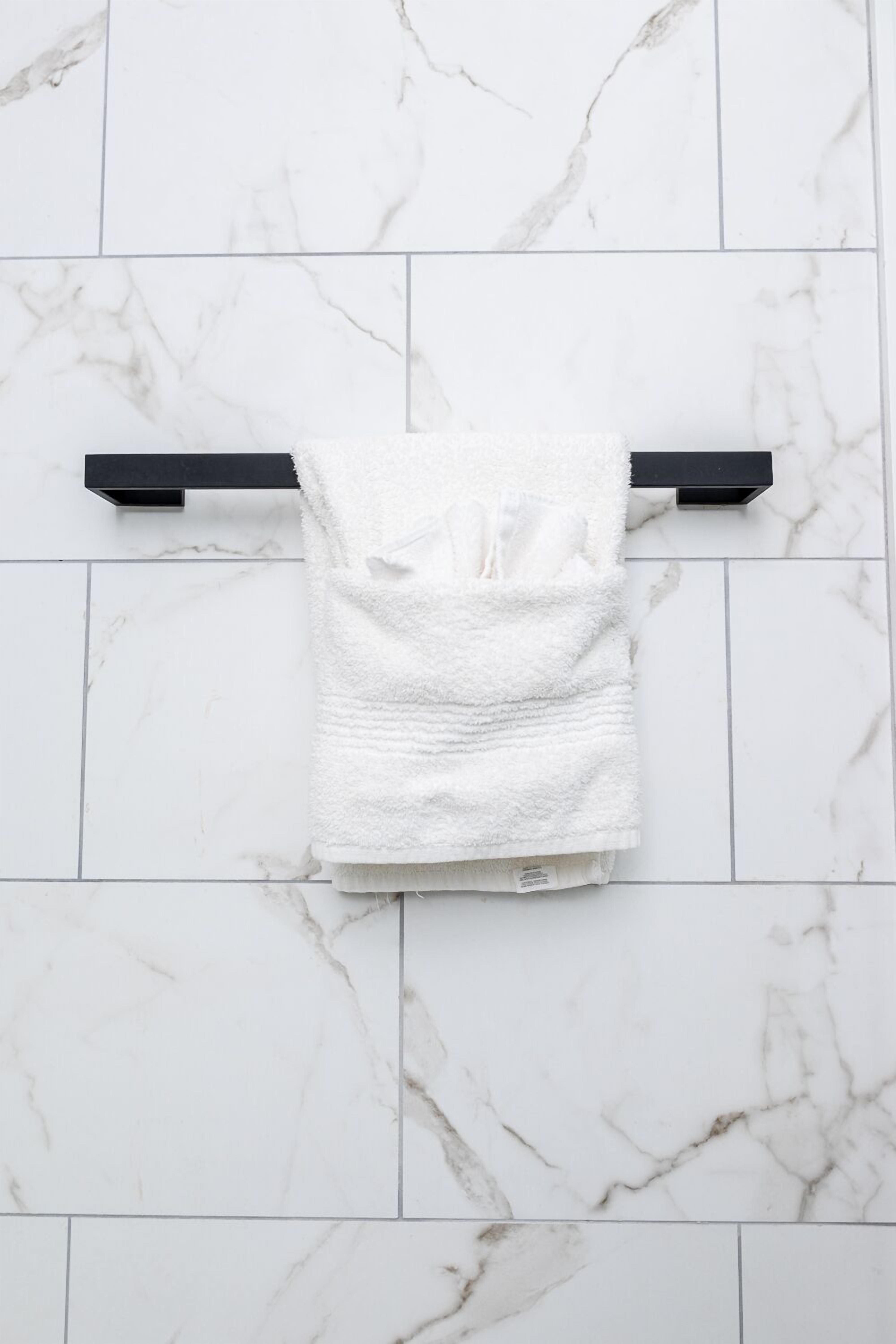Une serviette blanche est suspendue à un porte-serviettes noir, le tout se trouvant devant un mur recouvert de carreaux de marbre blanc.