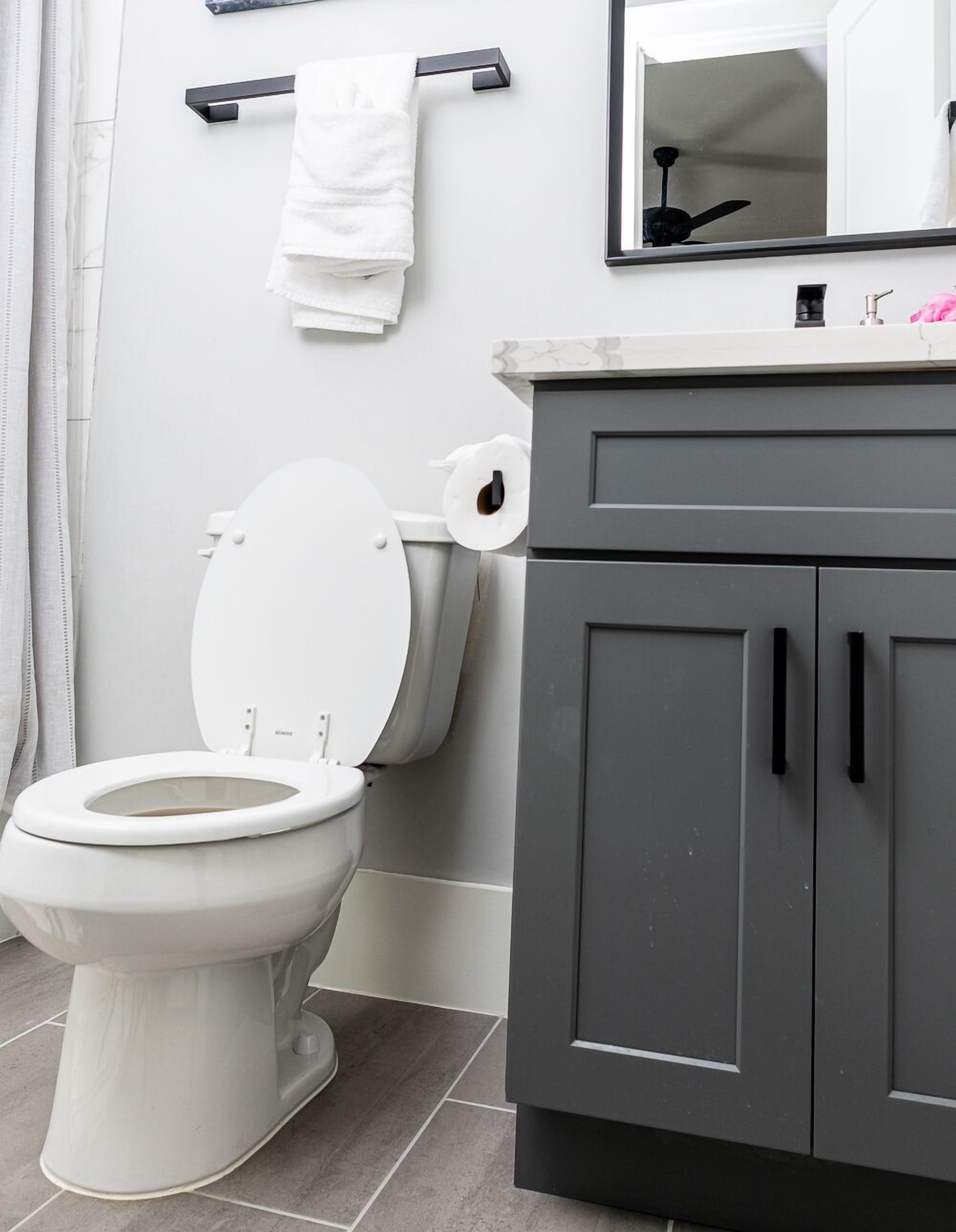 Et badeværelse med et hvidt toilet, grå skabe og en håndklæderadiator.