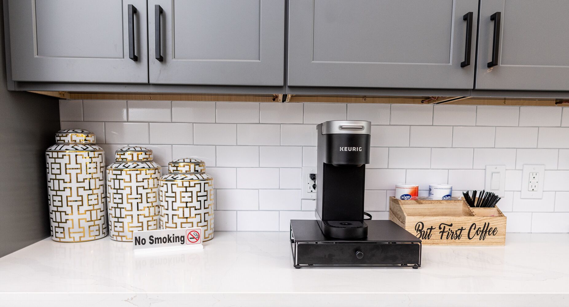 A kitchen with grey cabinets, a coffee maker, and three patterned containers.