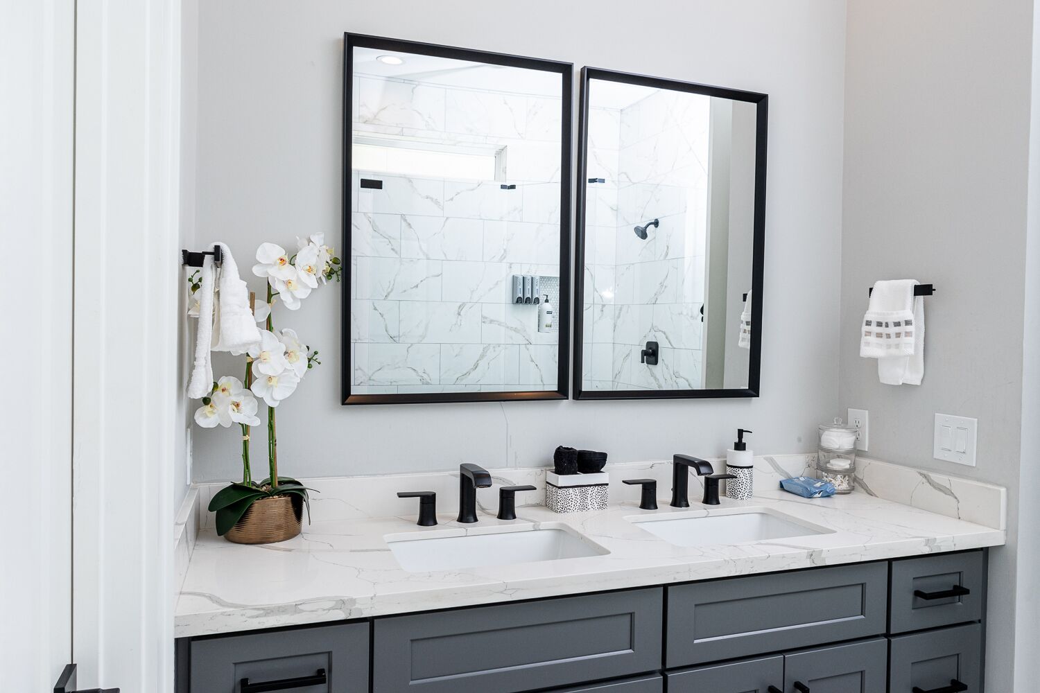 A modern bathroom with two mirrors, white marble countertops, and grey cabinetry.