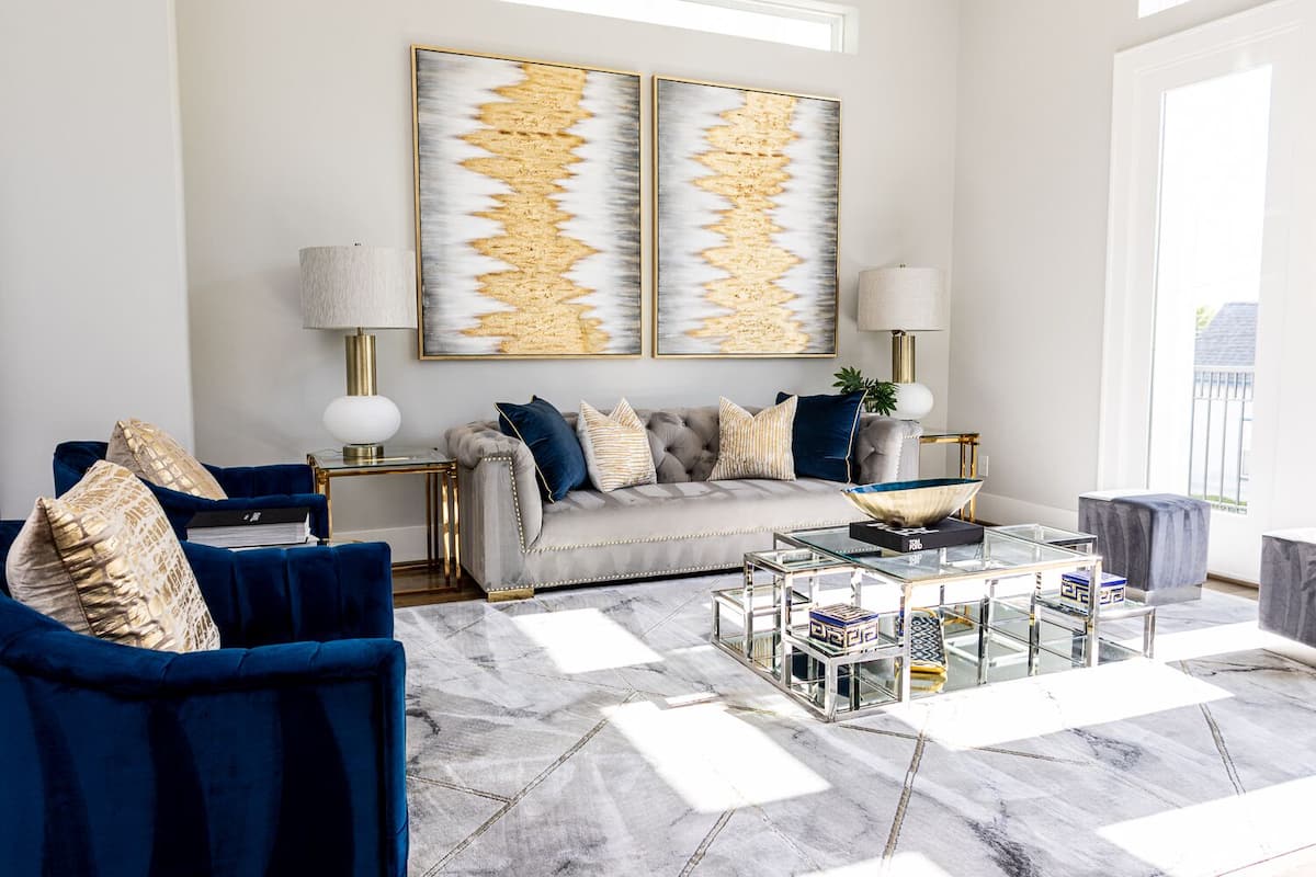 A modern living room with a grey sofa, blue armchairs, and a glass coffee table.
