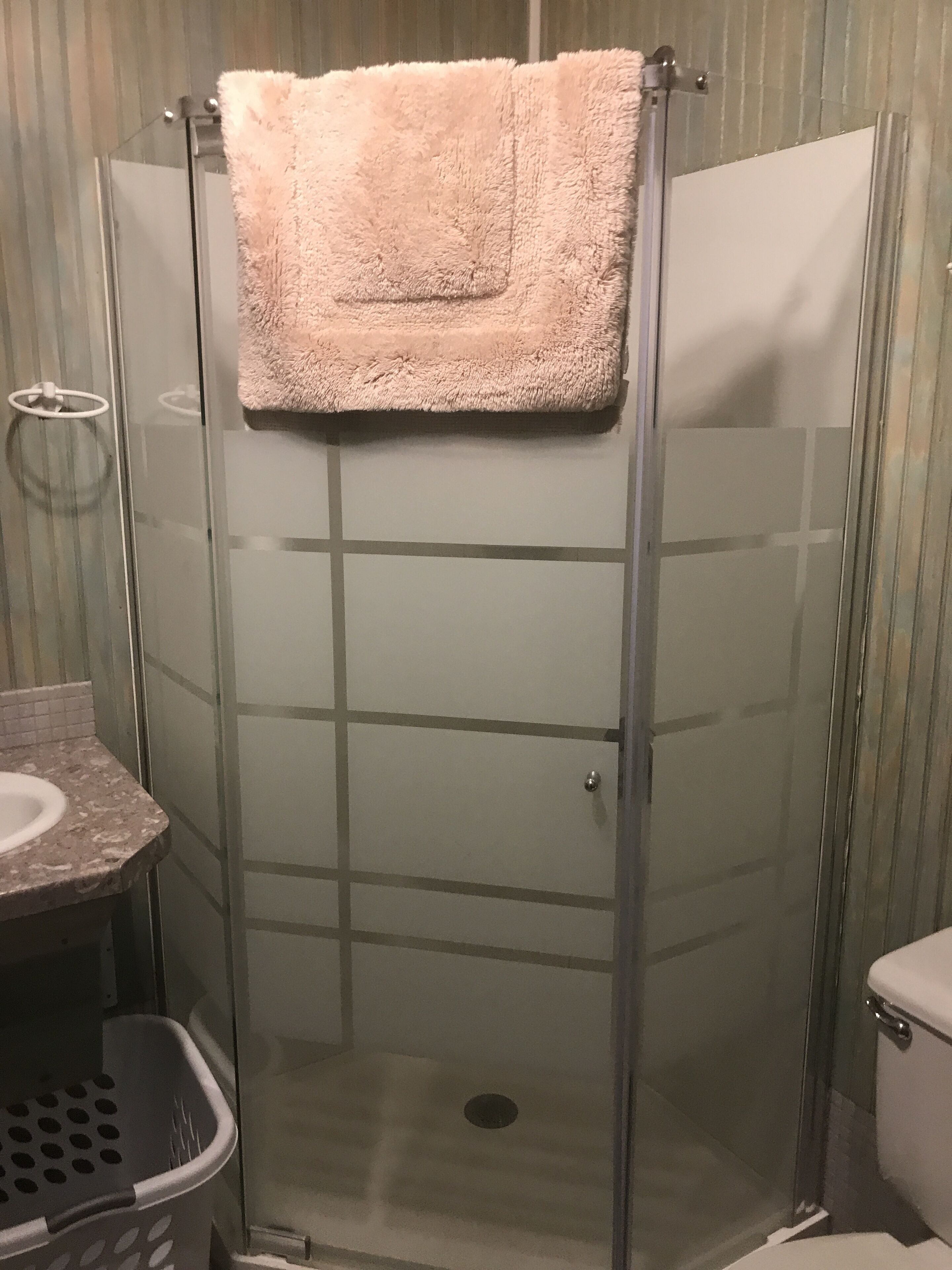A glass-enclosed shower stall with a beige towel hanging on the door handle.