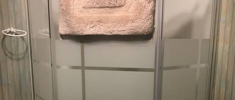 A glass-enclosed shower stall with a beige towel hanging on the door handle.