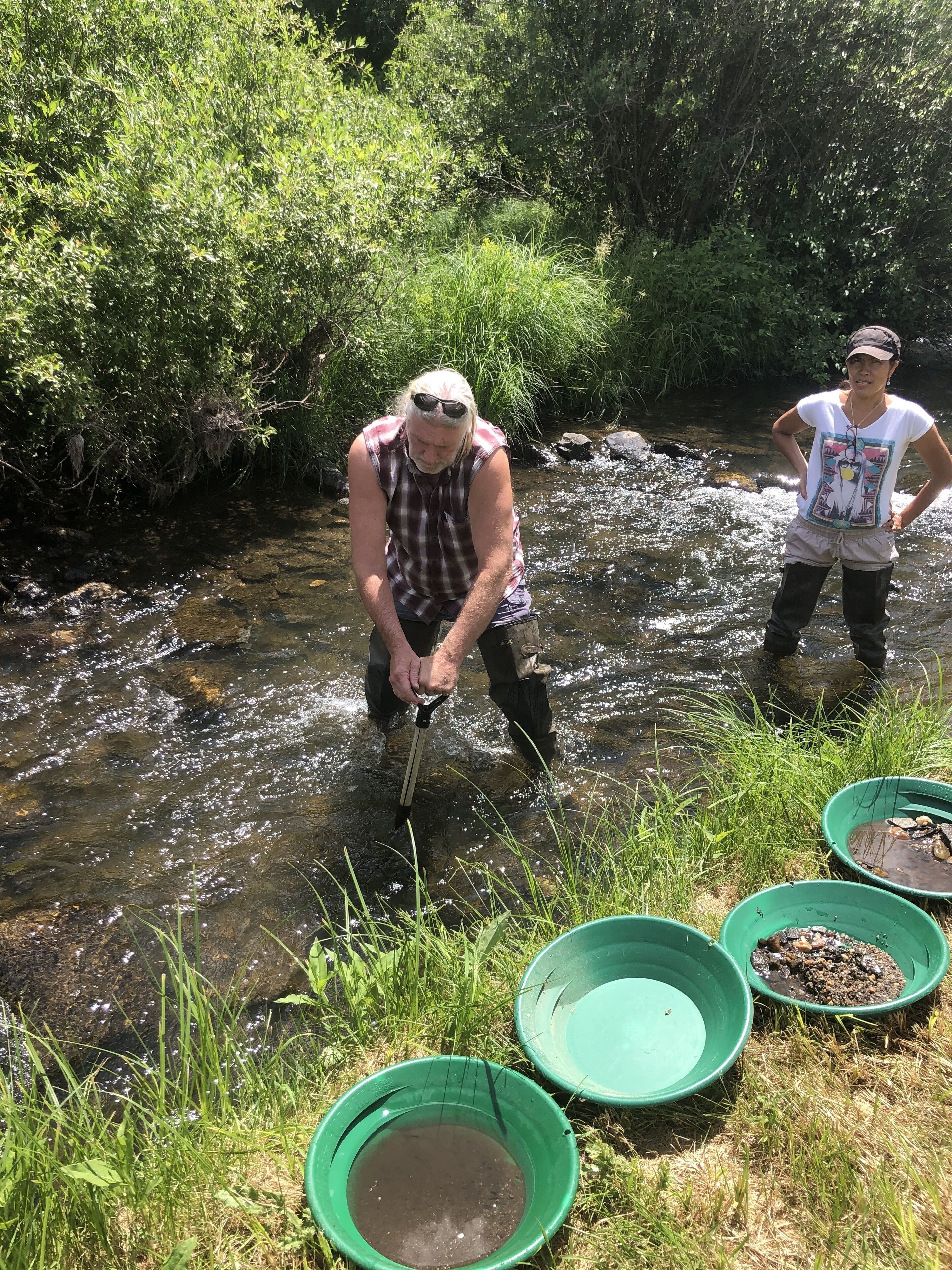 Two people by a stream with green buckets.