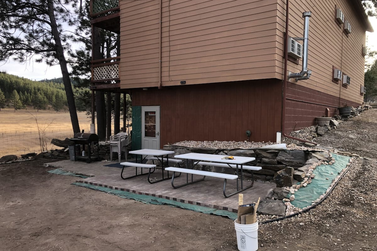 Eine Hütte mit einer Terrasse, die Picknicktische und einen Grillplatz bietet.