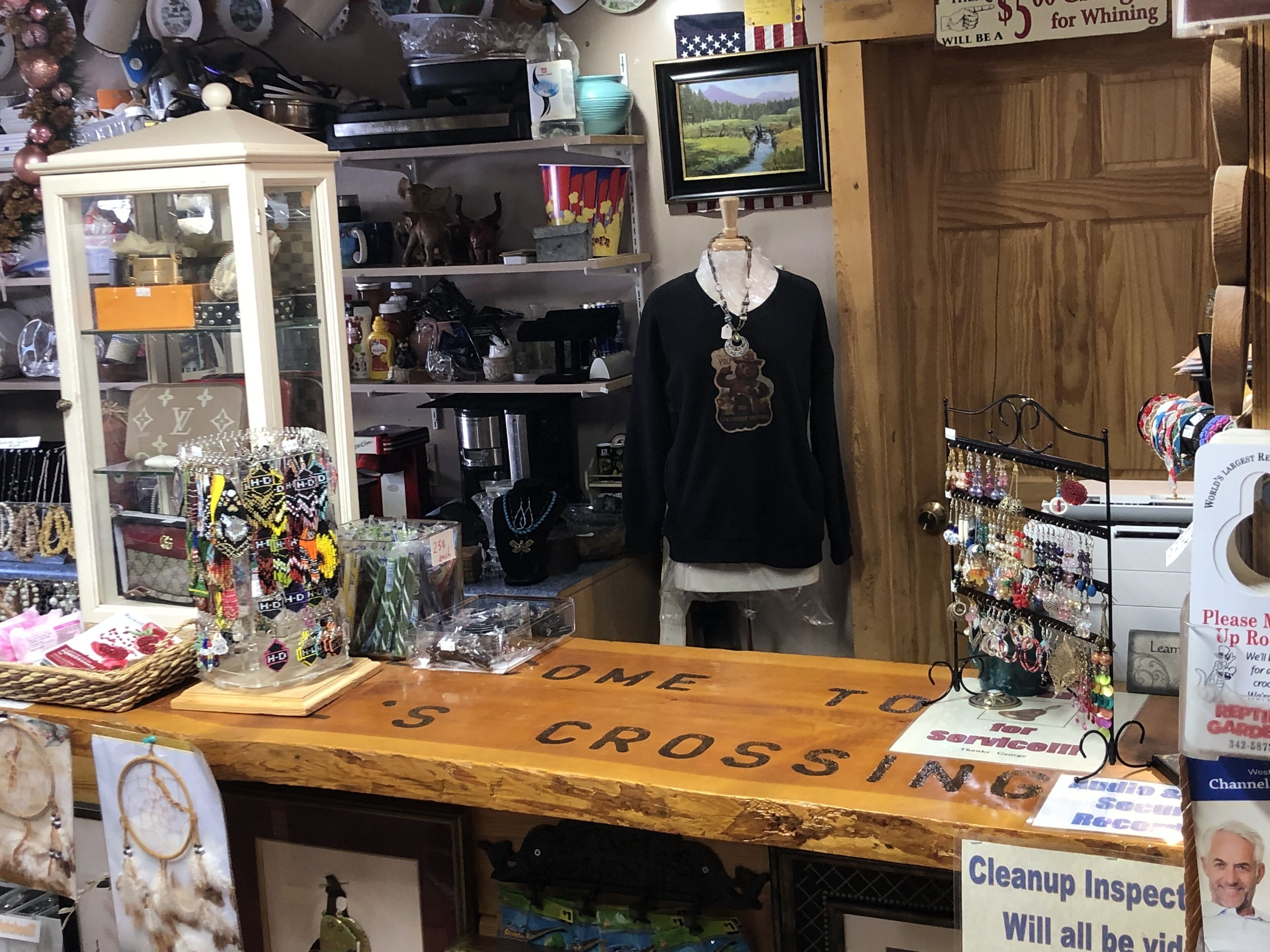 A cluttered shop with various items on shelves and a mannequin in the center.