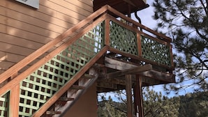 Una escalera de madera con barandilla de celosía verde que lleva a un balcón.