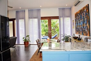A modern kitchen with a marble countertop, a dining area with a table and chairs, and a large window with curtains.
