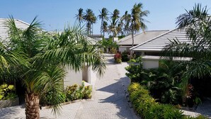A pathway leading to a building with a tiled roof, surrounded by palm trees and other greenery.