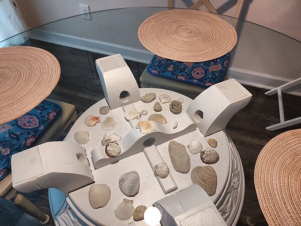 A round glass table with a white base, surrounded by blue patterned cushions and woven hats.