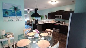 A modern kitchen with dark cabinets, a microwave, and a stove. There is a dining area with a table and chairs, and a painting of palm trees on the wall. - Beachy style and cosy. Book your own little hotel.No pet FEE, 4 Guests. (Sneads Ferry)