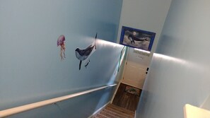 Una escalera con barandilla, una pared con un mural de delfín y medusa, y un cuadro enmarcado de ballena.