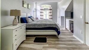 A bedroom with a bed, a dresser, a lamp, and a window with curtains. - Unit 27 | 4BR Home | 2 Mi to Disney | Pet Friendly | Gated Resort (Kissimmee)