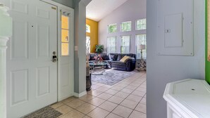 A spacious living room with a large sofa, a coffee table, and a view of the outside through large windows. - Unit 27 | 4BR Home | 2 Mi to Disney | Pet Friendly | Gated Resort (Kissimmee)