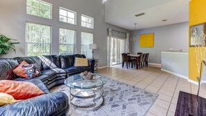 A spacious living room with a leather sofa, a glass coffee table, and a dining area with a yellow accent wall. - Unit 27 | 4BR Home | 2 Mi to Disney | Pet Friendly | Gated Resort (Kissimmee)
