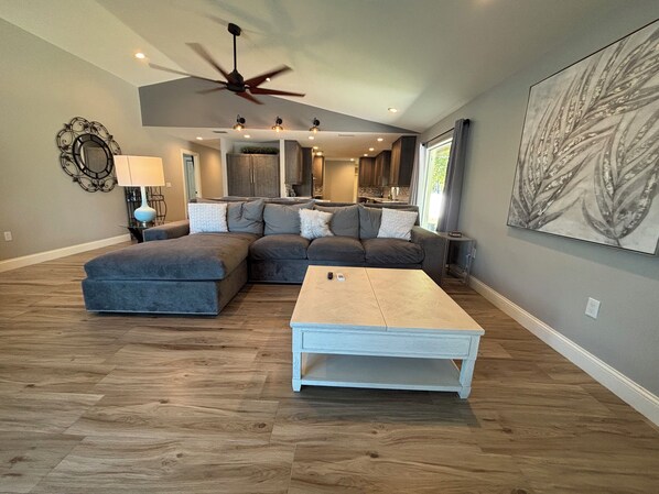 A modern living room with a sectional sofa, a white coffee table, and a ceiling fan.
