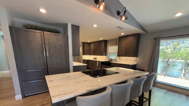 A modern kitchen with a central island, bar stools, and a view of the outdoors.