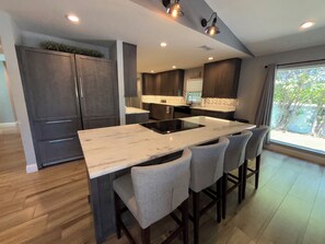 A modern kitchen with a central island, bar stools, and a view of the outdoors.
