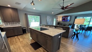 A modern kitchen with a central island, wooden flooring, and a dining area with a round table and chairs.