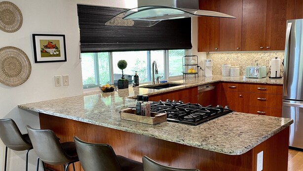 A modern kitchen with a large island, bar stools, a stainless steel range, and a built-in oven. - 6BR-Spacious-Bright-Modern (Eugene)