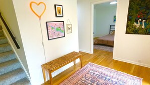 A room with a wooden floor, a bench, a colorful rug, a heart-shaped neon light, and a painting on the wall. - 6BR-Spacious-Bright-Modern (Eugene)