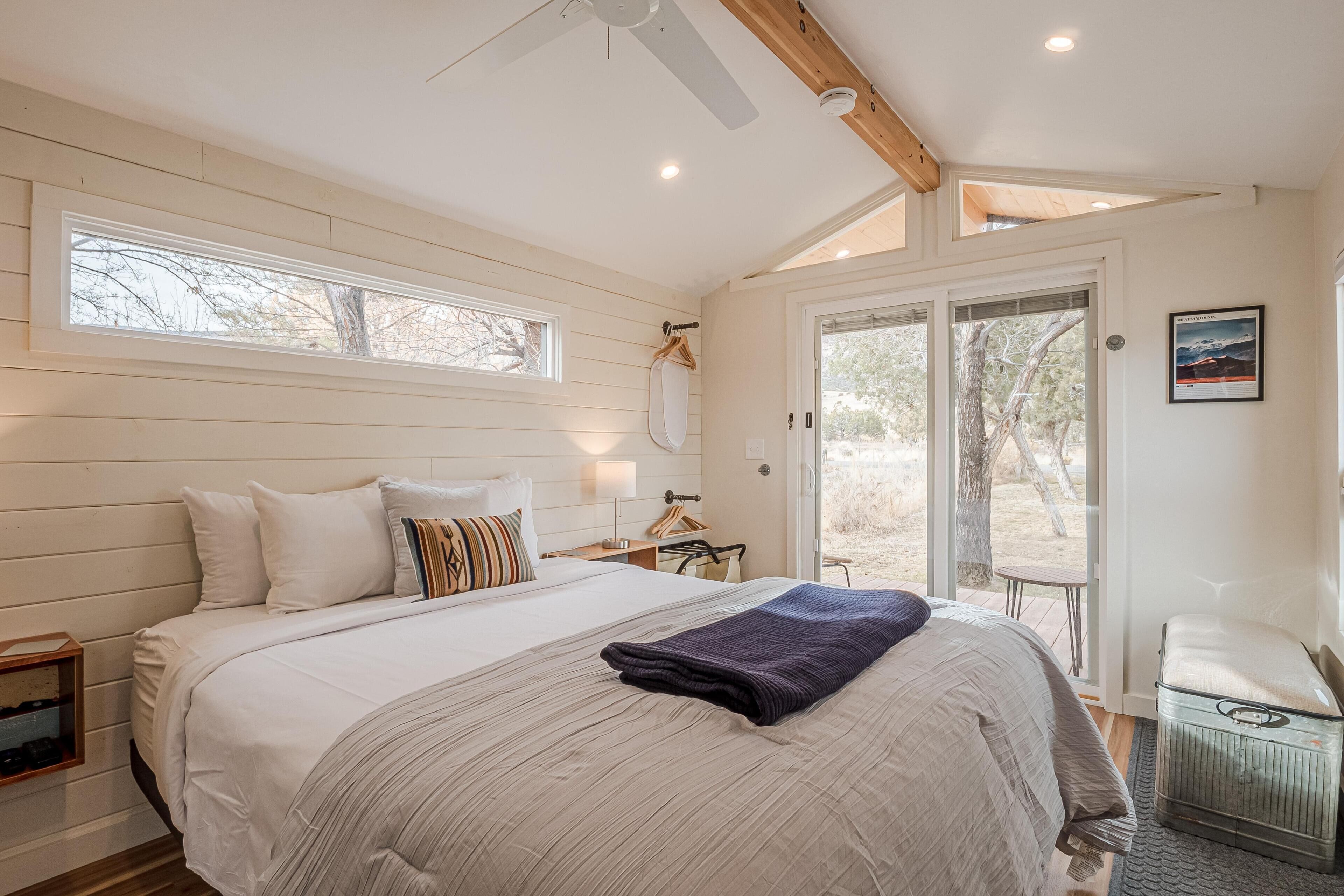 A bedroom with a large bed, a ceiling fan, a window, and a door leading to an outdoor area.