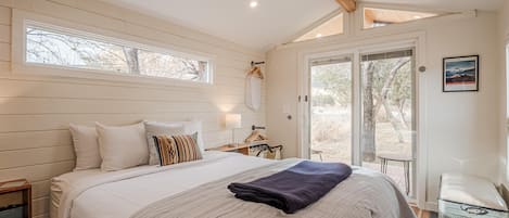 Quarto com cama grande, ventoinha no teto, janela e porta que dá para uma área externa.