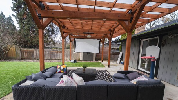 Eine Außenpatio mit überdachter Sitzgelegenheit, einem Basketballkorb und einer Garage im Hintergrund.