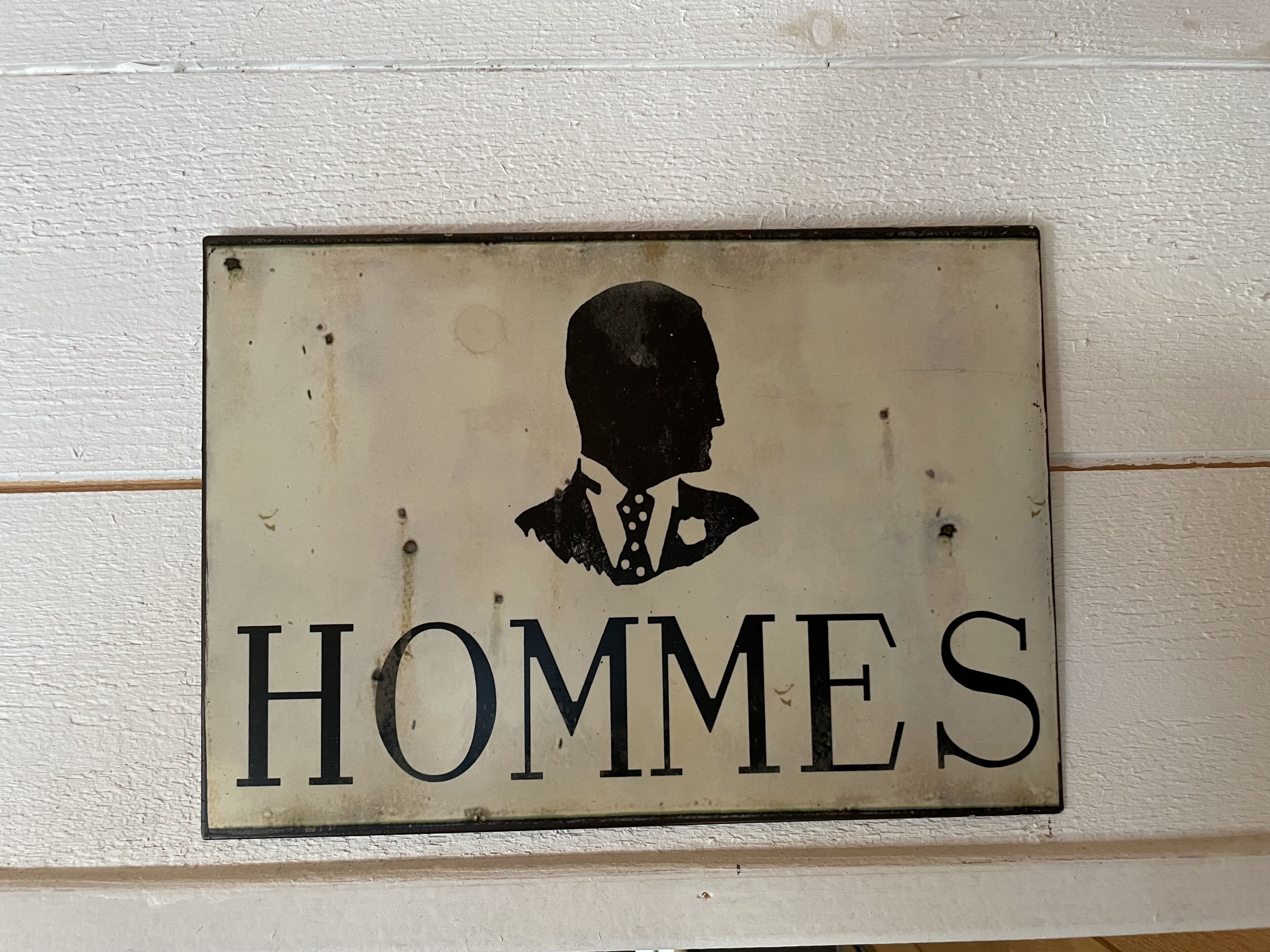 Opastekyltti, jossa on miehen siluetti ja sana ”HOMMES” valkoisella pohjalla.