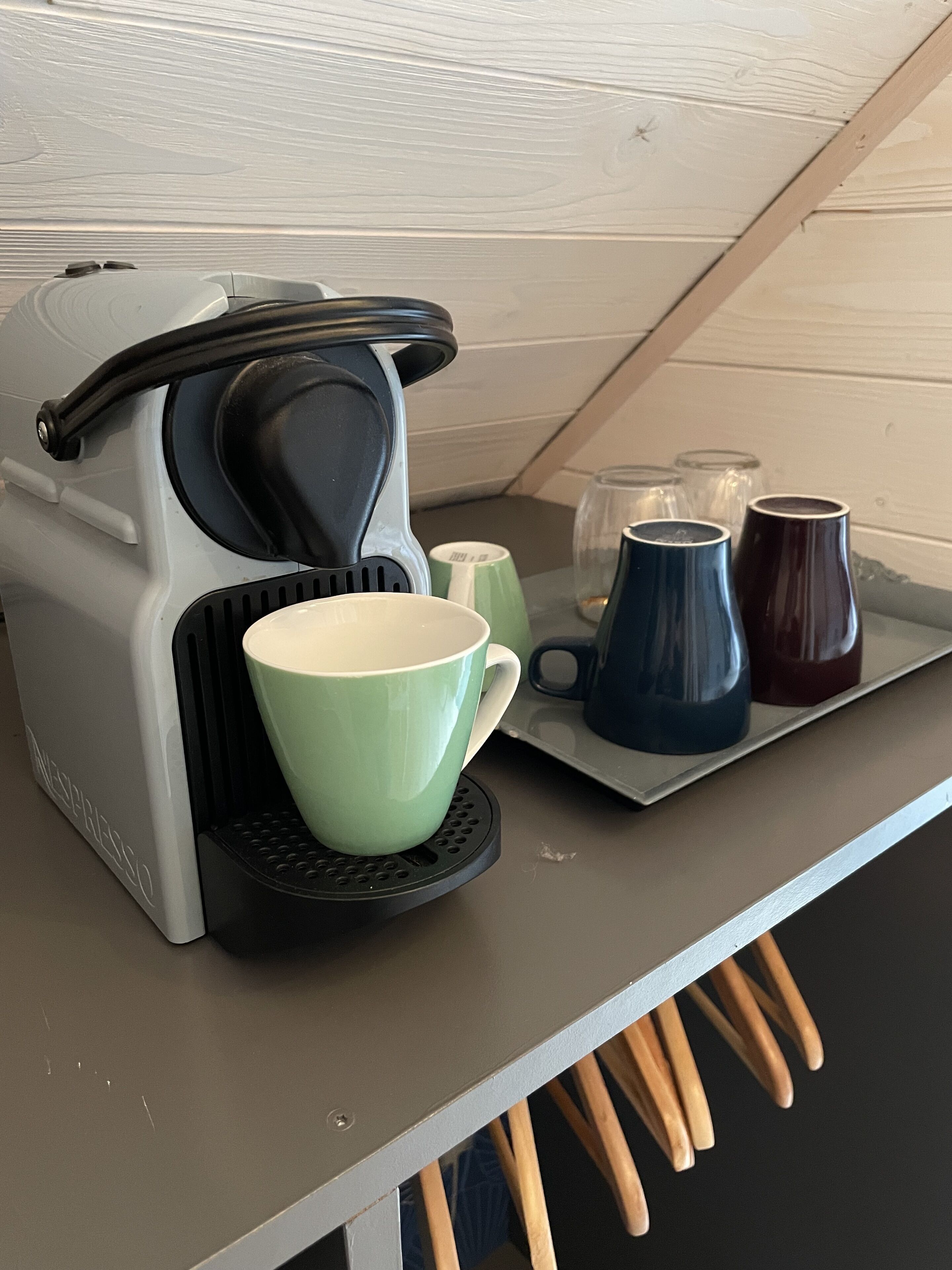 Una cocina con cafetera, una taza verde y varias tazas en una bandeja.