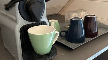 Una cocina con cafetera, una taza verde y varias tazas en una bandeja.