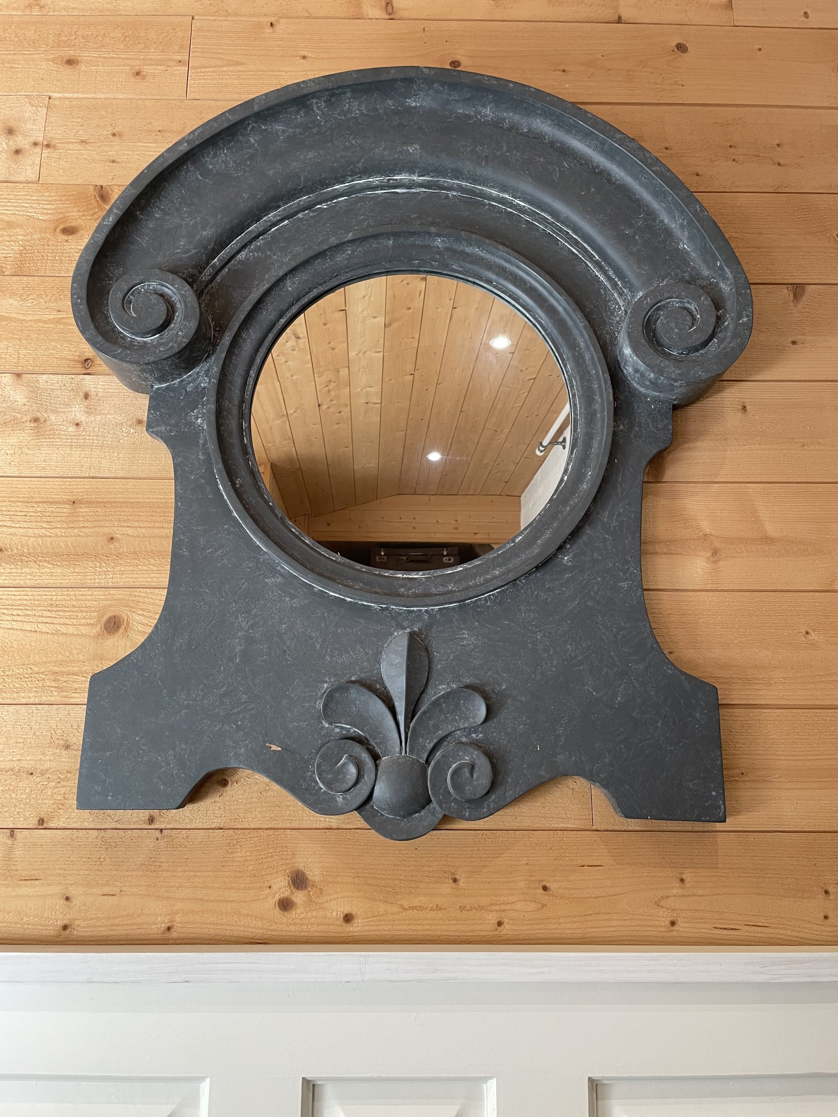 A black, ornate mirror with a circular center and decorative elements, mounted on a wooden wall.