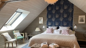 Een slaapkamer met een schuine plafond, een groot bed met opvallende kussens, een bank met handdoeken, een hondenbeeld en een dakraam.