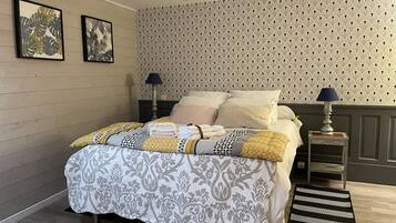A neatly made bed with a patterned bedspread and pillows, a bedside table with a lamp, and a decorative wall with a repeating pattern.