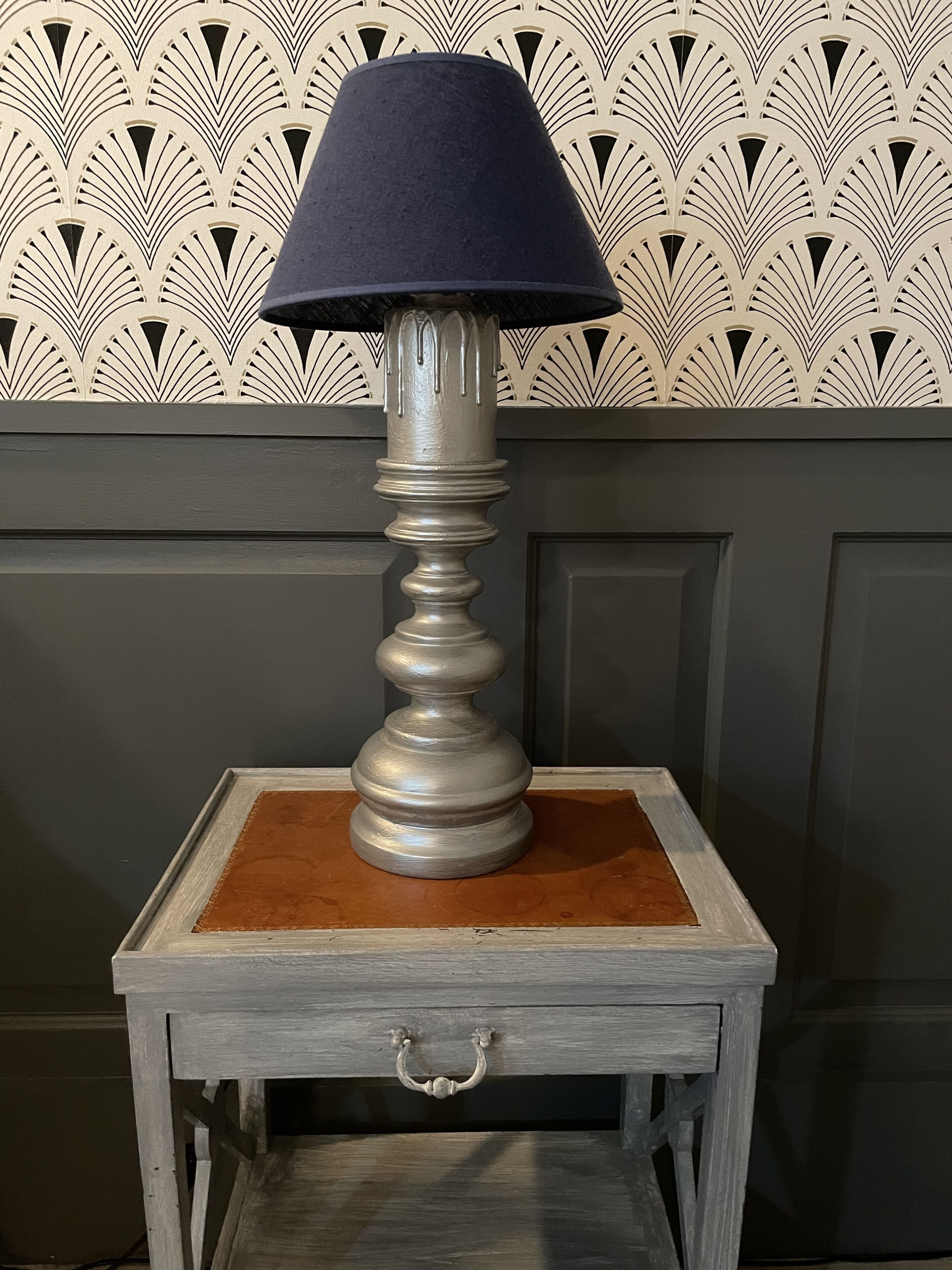 A table lamp with a dark shade on a wooden table with a drawer.