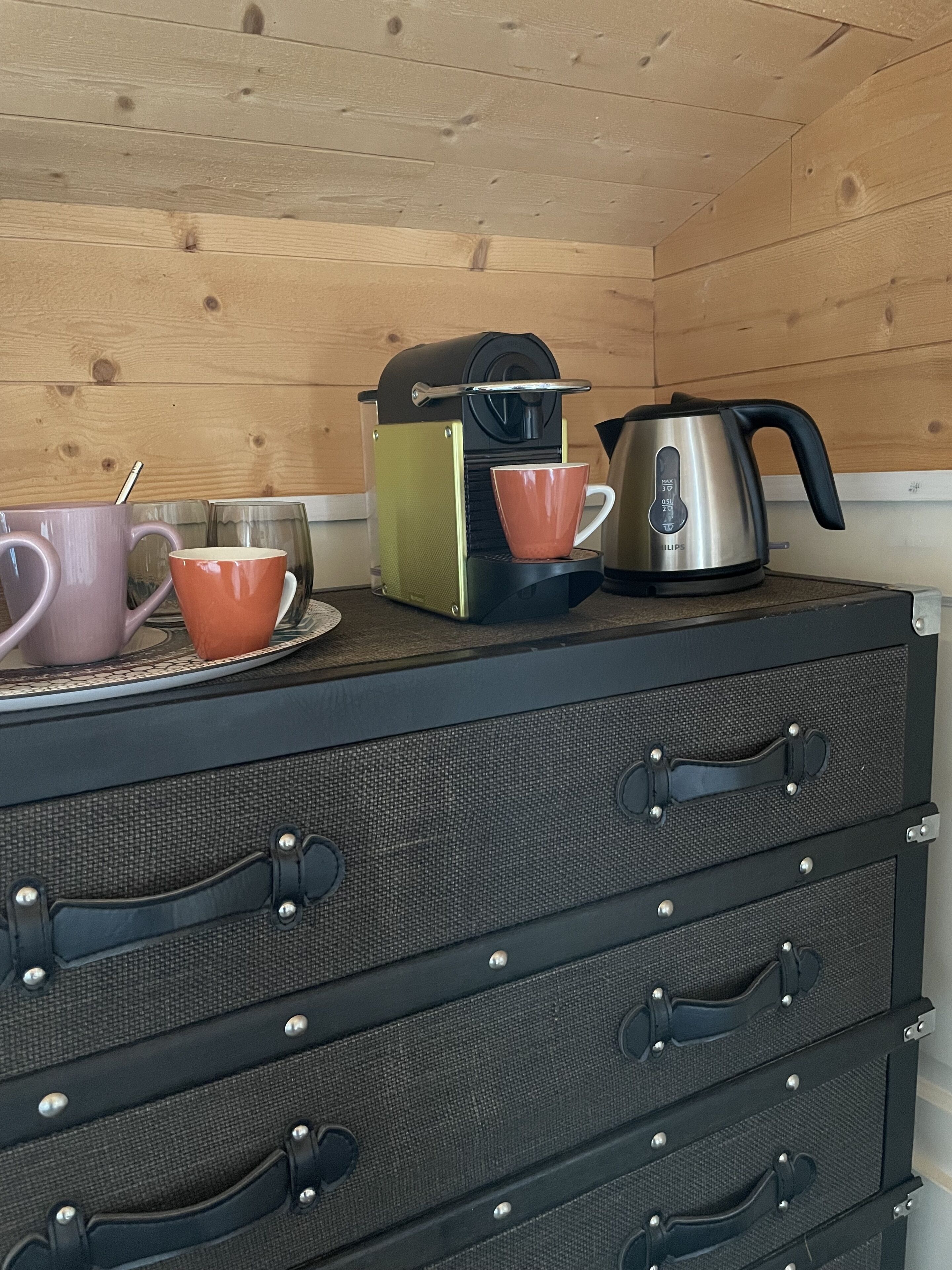 Uma cozinha compacta com cafeteira, chaleira e duas xícaras em uma bancada.