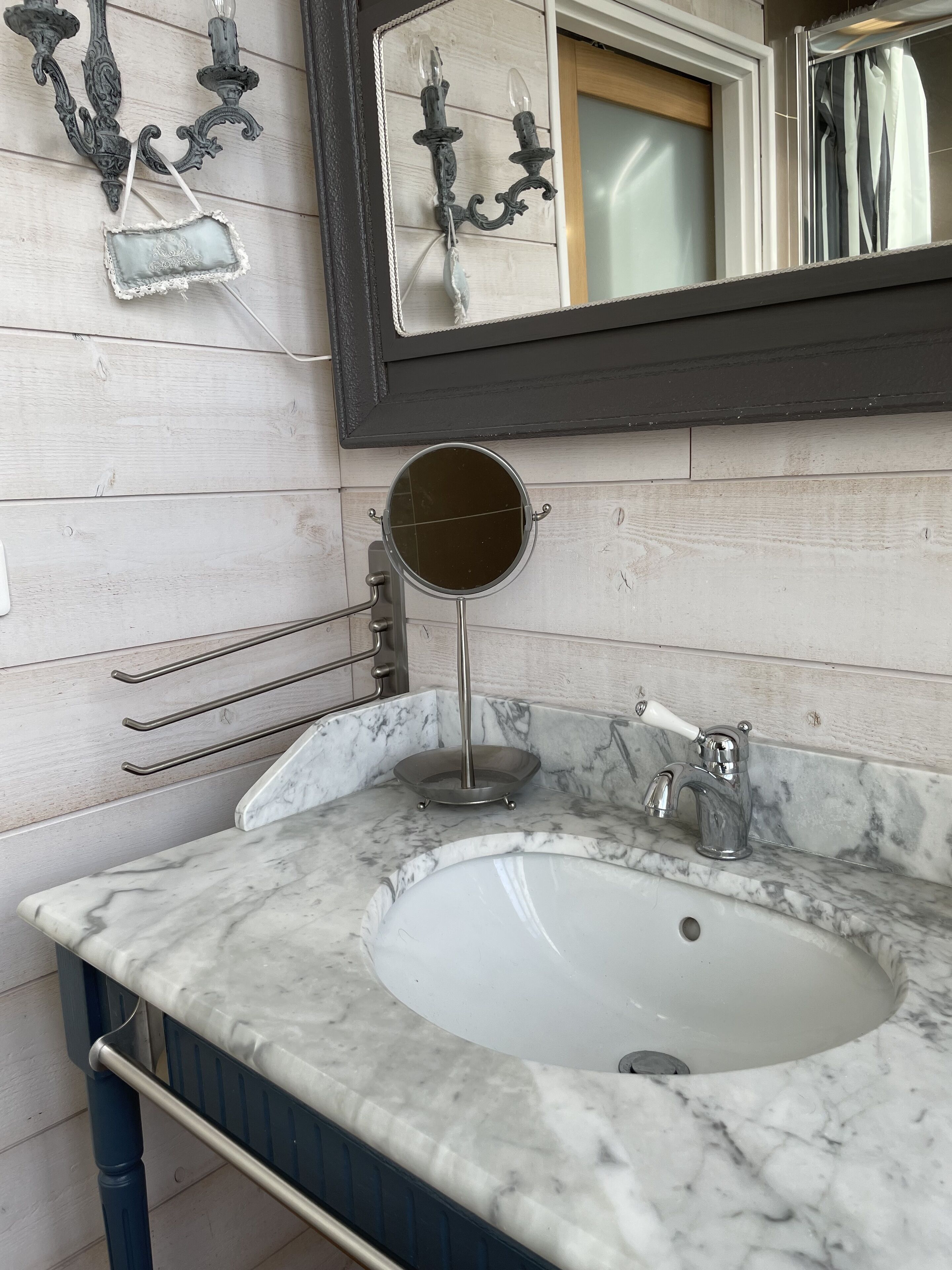 A bathroom with a marble sink, a round mirror, and a wall-mounted light fixture.