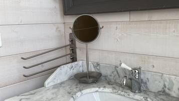 A bathroom with a marble sink, a round mirror, and a wall-mounted light fixture.