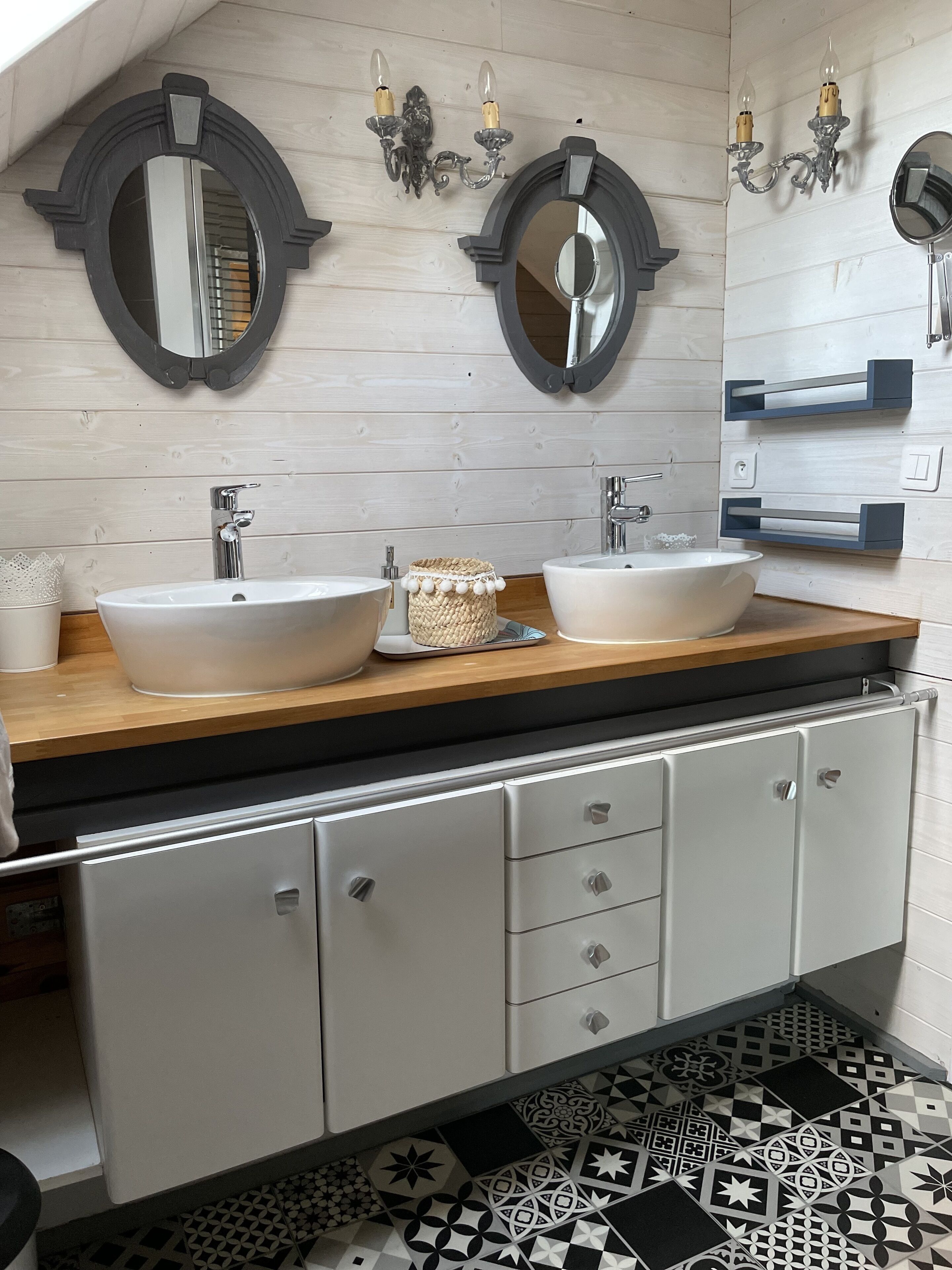 Un baño moderno con dos lavamanos blancos, encimera de madera y un espejo decorativo sobre cada lavamanos.