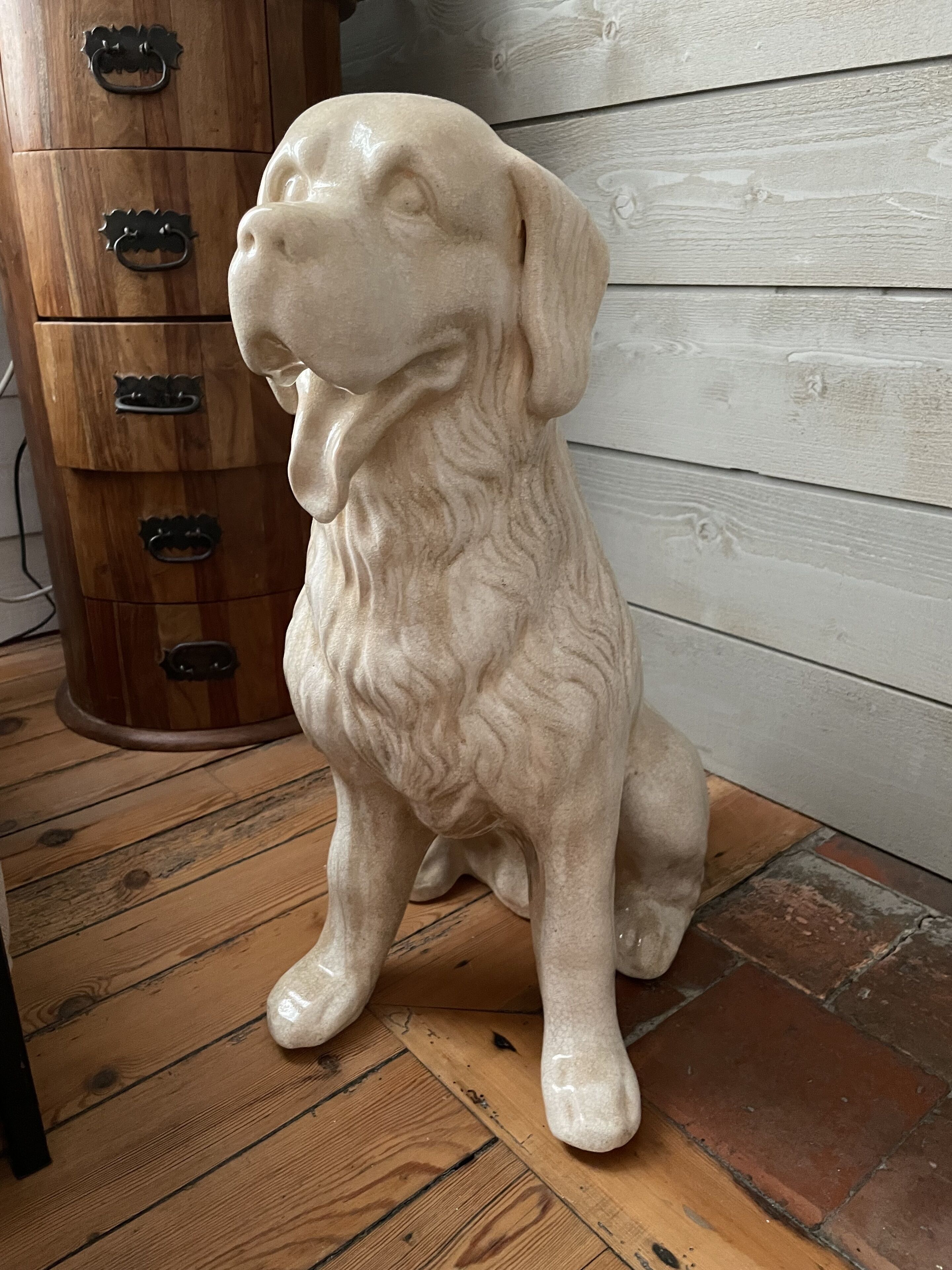 Uma estátua de mármore de um cão sentado sobre um piso de madeira.