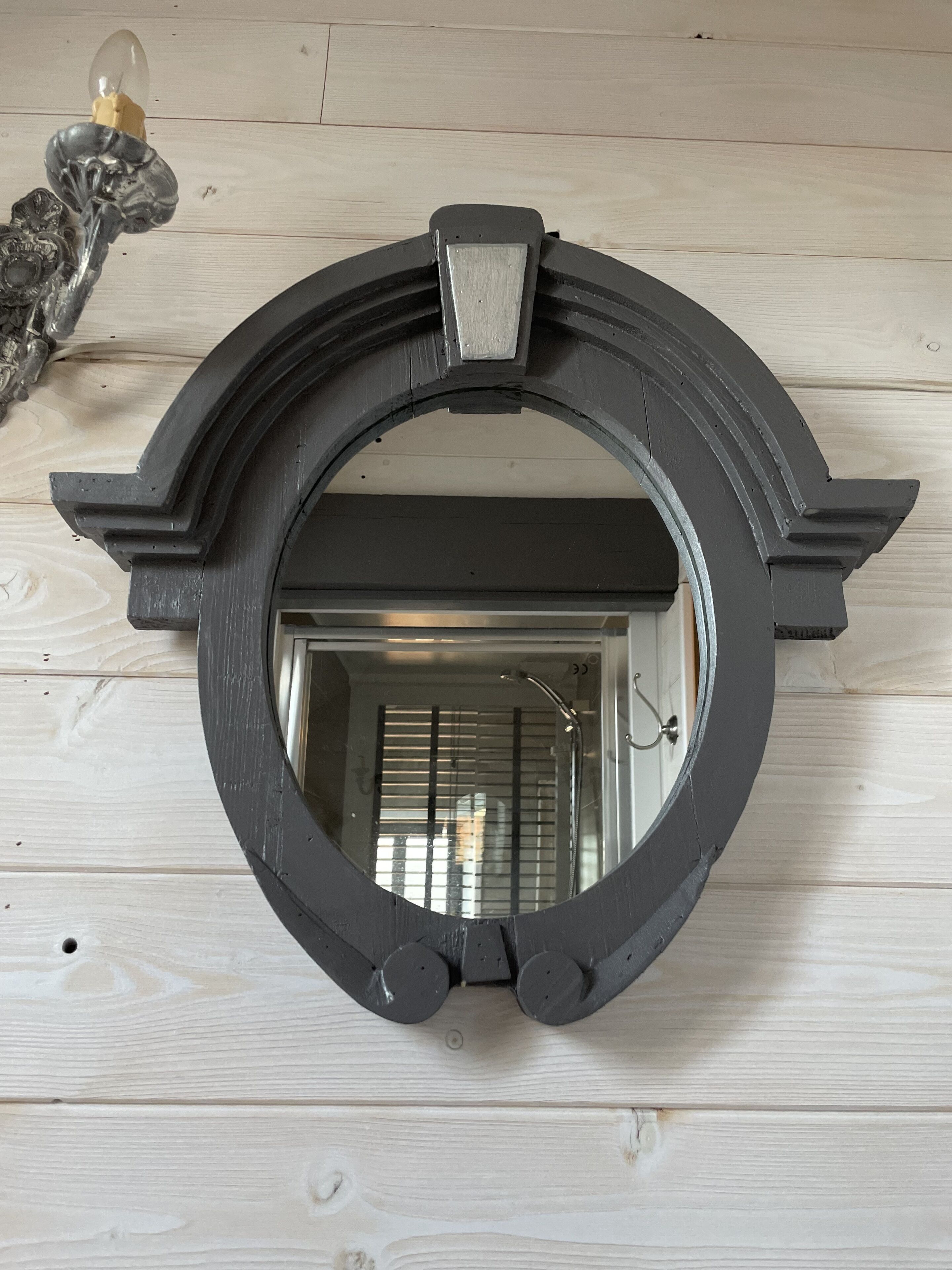 A round mirror with a black frame mounted on a wooden wall.