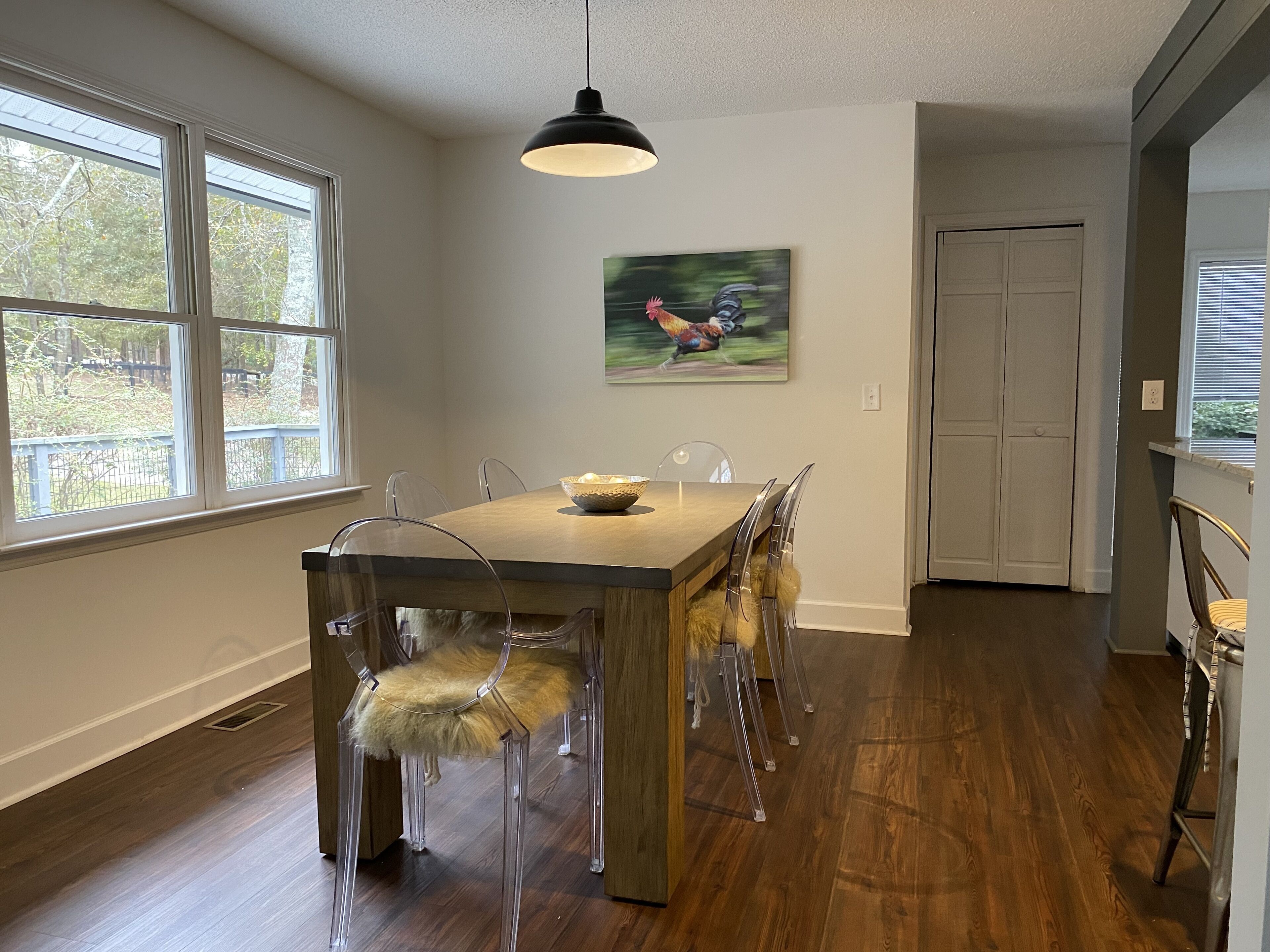 A dining area with a wooden table, clear chairs, and a black pendant light.