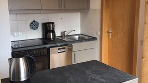 Et kompakt køkken med en sort bordplade, rustfrie hvidevarer og en trädør.