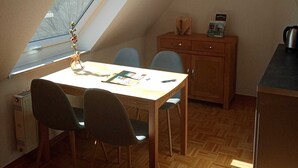 Et værelse med skråvæg, ovenlys, et træbord med stole, et lille skab og en radiator.