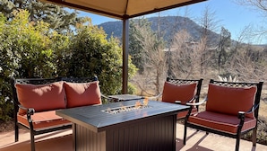 Eine Terrassengruppe im Freien mit Feuerschale und zwei Stühlen, umgeben von Grünpflanzen und Blick auf die Berge.