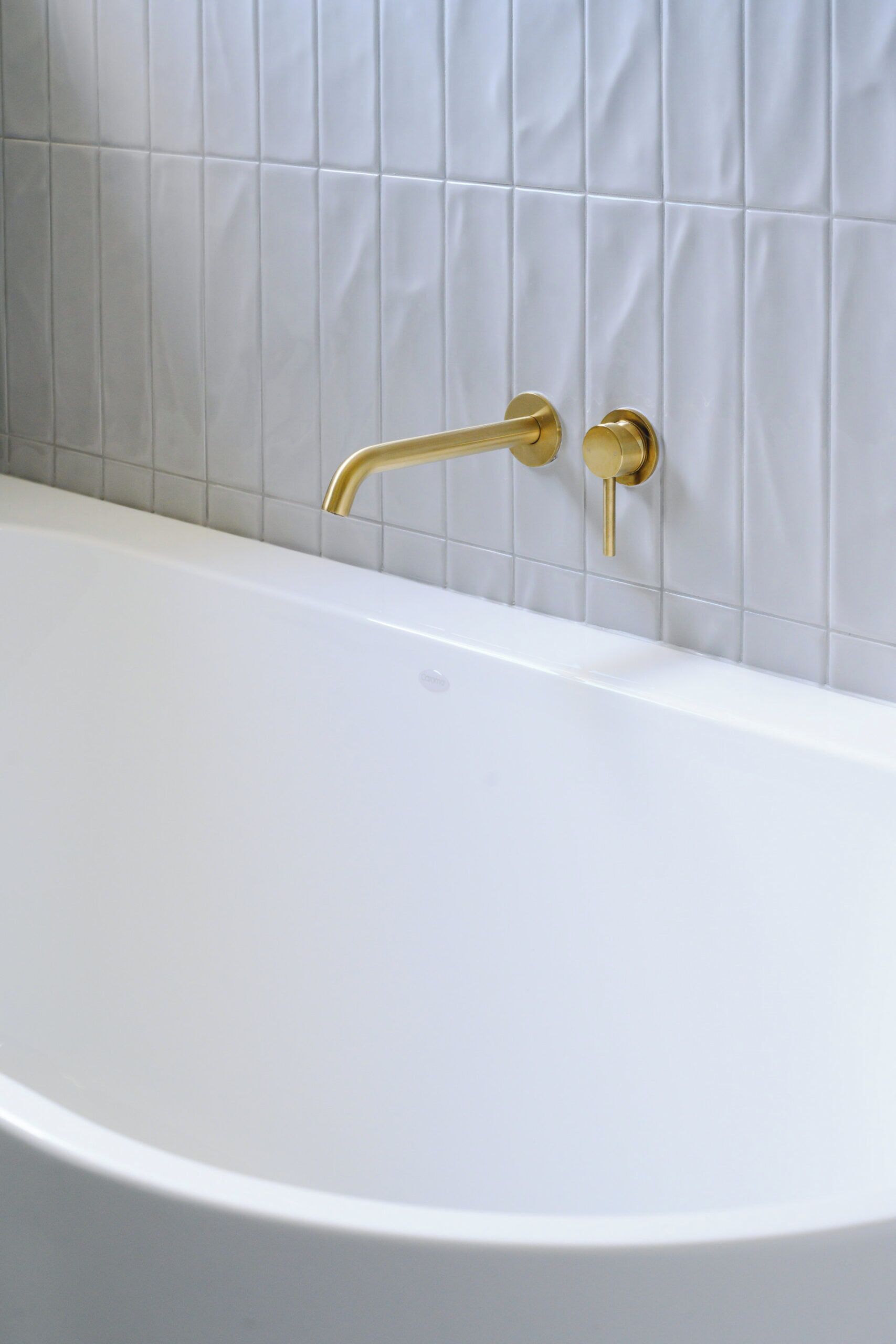 Une baignoire blanche, avec un robinet doré et une poignée dorée, placée devant un mur carrelé.